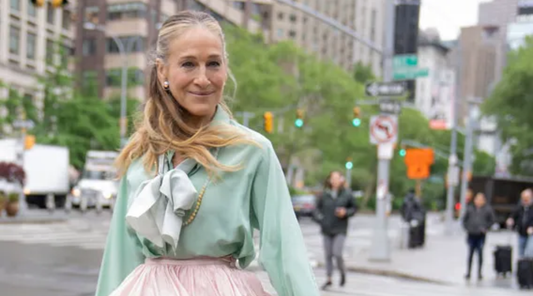 Sarah Jessica Parker with her grey blended hair pulled back wearing mint coloured blouse and pink ruffled skirt
