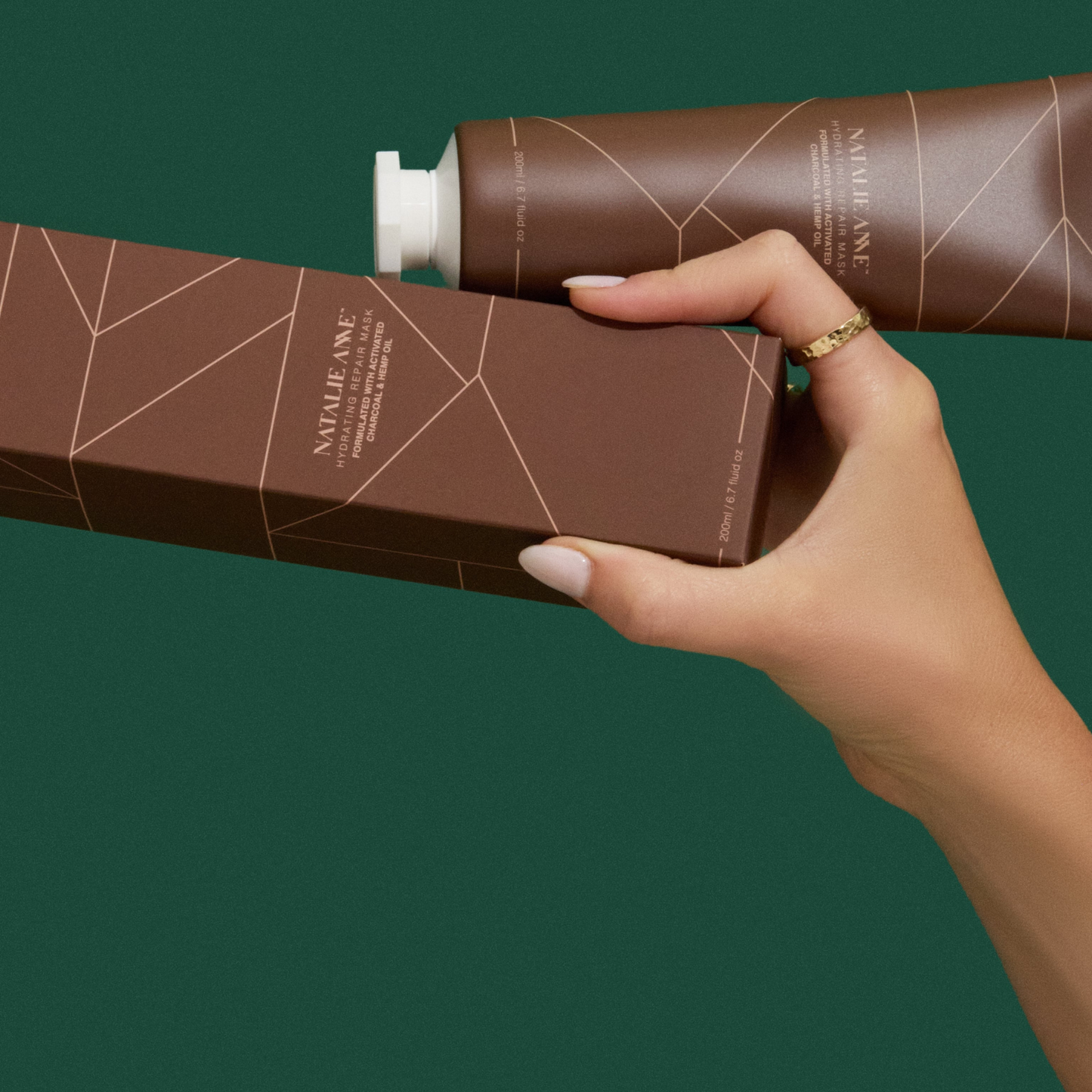 Hand holding Natalie Anne Hydrating Repair Mask against a green background