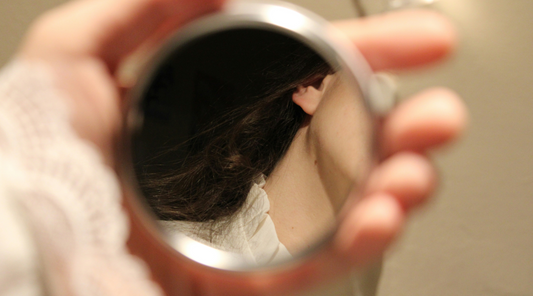 Woman looking in circular pocket mirror at her hair