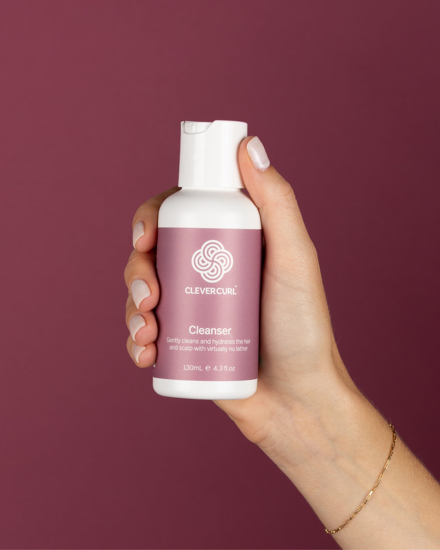 Hand holding a bottle of Clever Curls 130ml Cleanser against a purple background