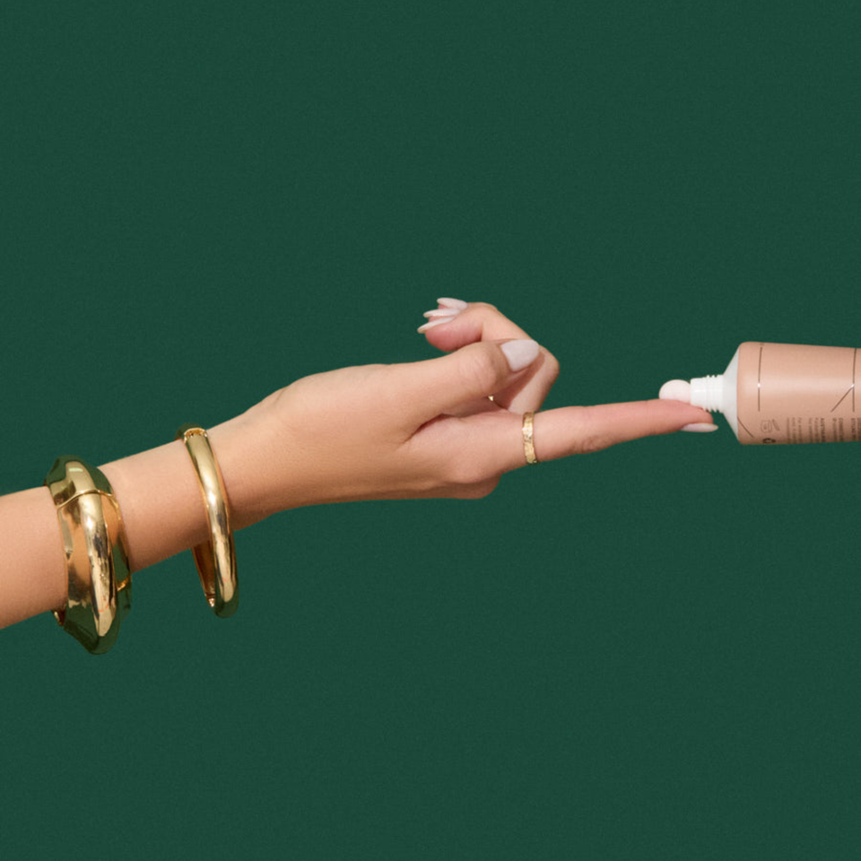 Natalie Anne Prep & Play All-In-One Cream being squeezed onto finger tip on green background