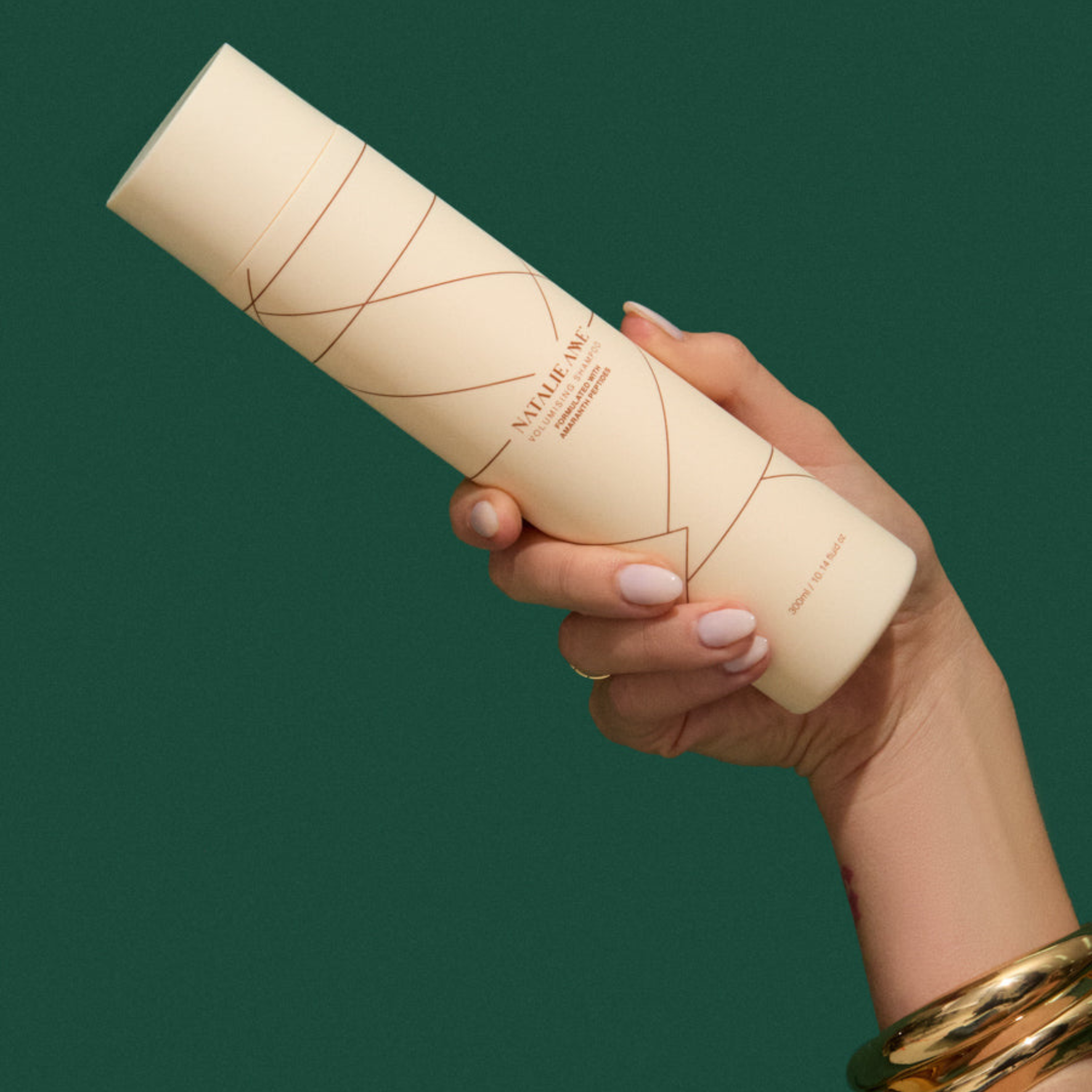 hand holding Natalie Anne Volumising Shampoo on green background