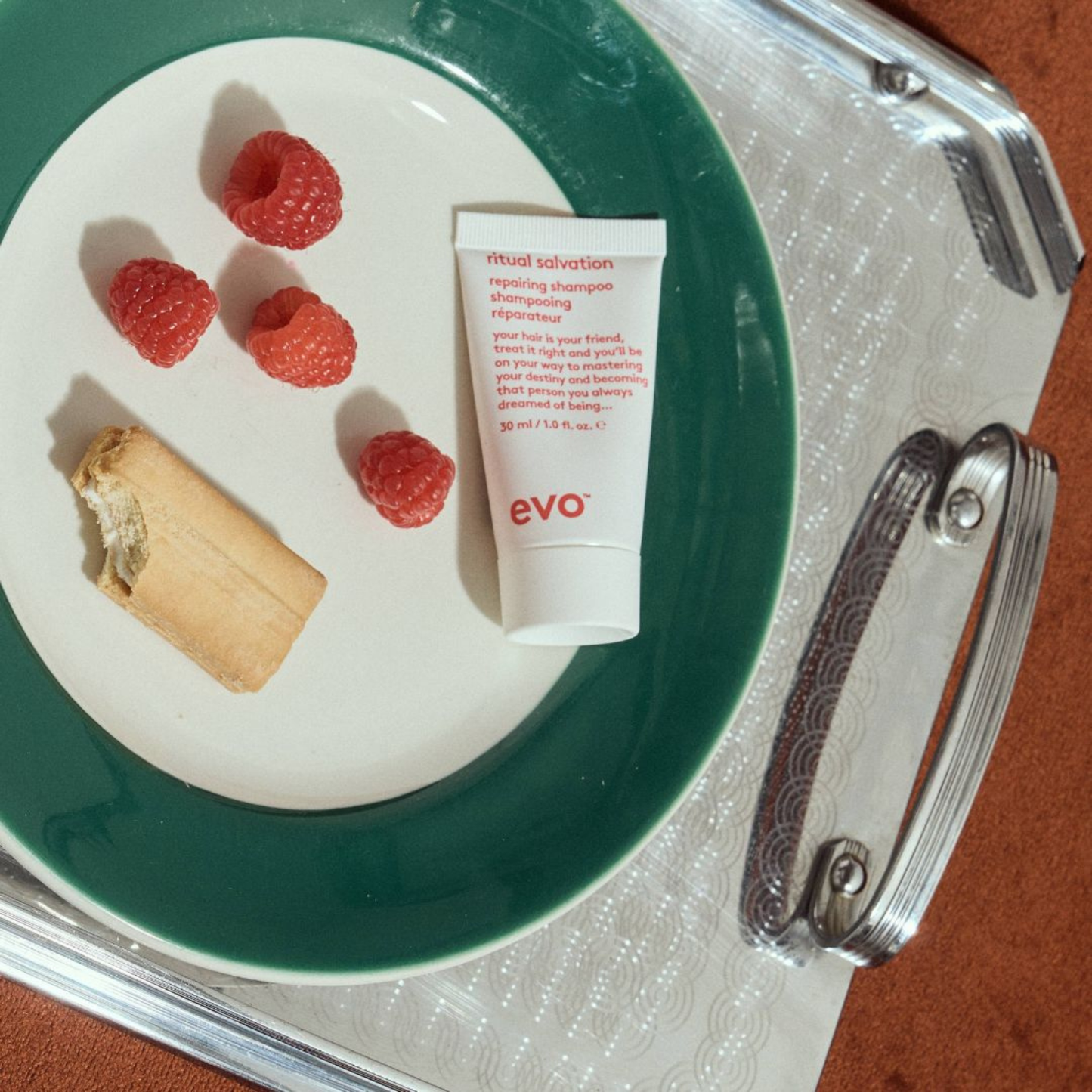 Tube of evo ritual salvation repairing shampoo on a plate with raspberries and a cracker, on a tray.